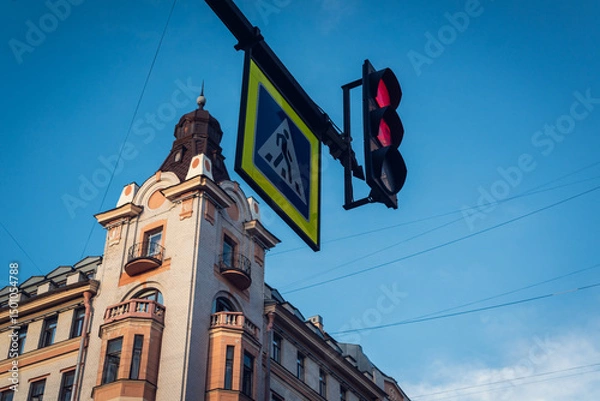 Fototapeta Traffic light and crossing sign against the backdrop of blue sky and a beautiful historic facade in the city of St. Petersburg.