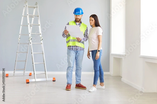 Fototapeta Man construction industry engineer and builder in uniform and hardhat and young woman homeowner talk about home remodeling, discuss house renovation, and develop indoor living space redesign project