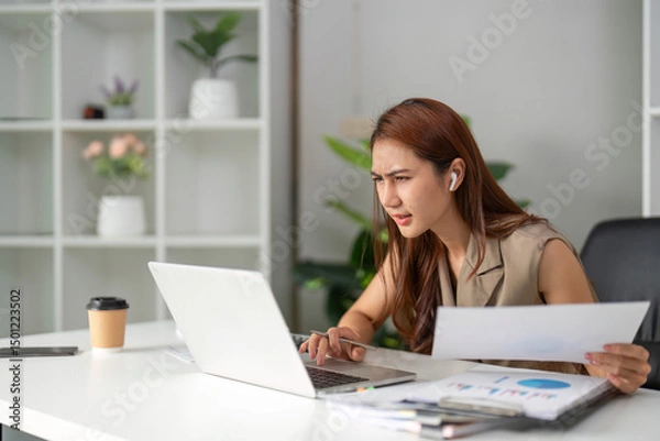 Fototapeta Work Online and Problem Solving. A young professional appears focused and concerned while navigating complex documents in a remote setting.