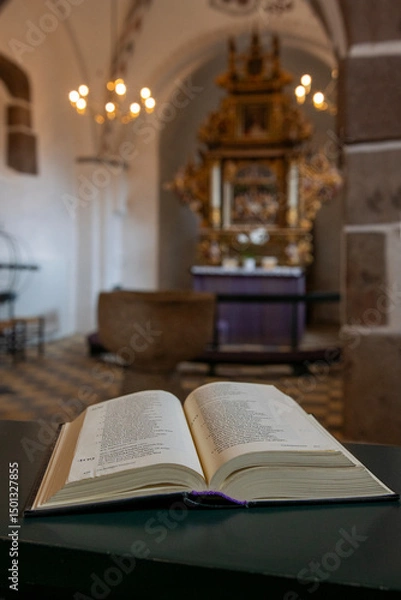 Fototapeta An open holy book rests at the front, gazing out over the church, where the chandelier glimmers above the nave
