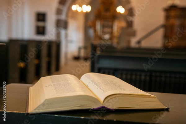 Fototapeta An open holy book rests at the front, gazing out over the church, where the chandelier glimmers above the nave