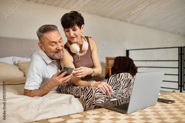 Fototapeta Happy couple enjoying a cozy moment together at home with tech