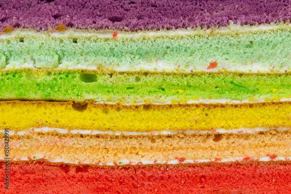 Fototapeta Texture of a vibrant rainbow cake slice, showcasing distinct layers of red, orange, yellow, green, light green, and purple sponge separated by creamy white frosting.