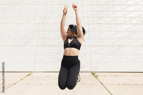Fototapeta A happy young woman jumps in the air, while listening to music and enjoys a time of sport and disconnection