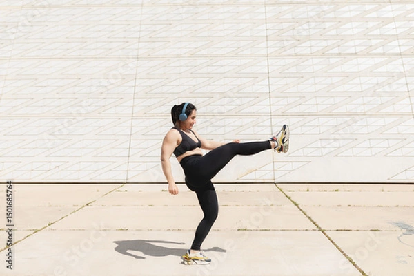Fototapeta A woman kicks her leg in the air while enjoying some time in the sun after exercising