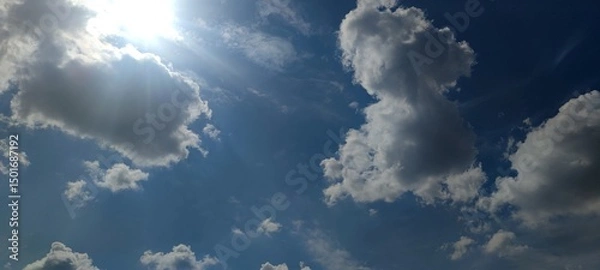Fototapeta White multi-level clouds. Snow-white fluffy cumulus and translucent cirrus clouds in the light blue sky. They are located at different heights. The bright sun shines from behind the cloud.