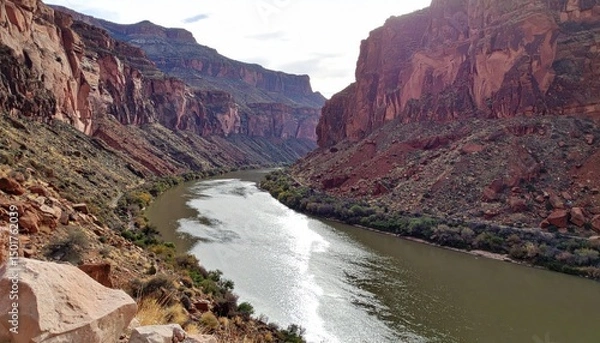 Fototapeta Deep river flows through tall, layered canyon walls under a partly cloudy sky