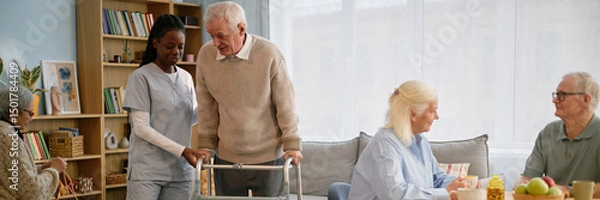 Fototapeta Caregiver assisting senior man using walker. Elderly people sitting, chatting, and enjoying meal at table in comfortable care home environment
