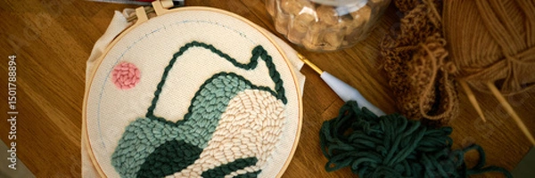 Fototapeta Detailed view of an ongoing embroidery project, showcasing a landscape pattern and yarn organized around Embroidery hoop placed on wooden table, highlighting hand craftsmanship