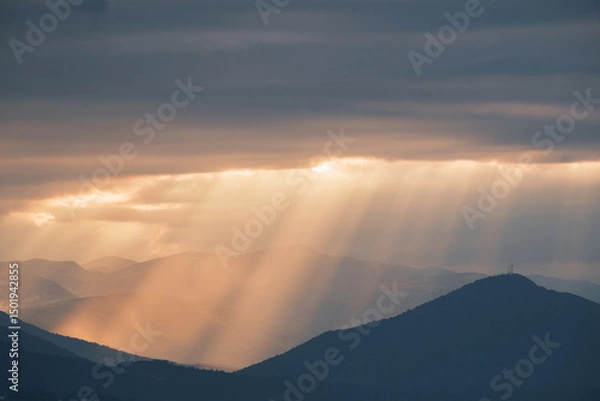 Fototapeta Mountain vista with sunbeams piercing through the clouds creating a serene and dramatic atmosphere