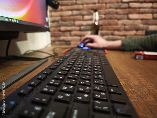 Fototapeta Close up of a black keyboard on a wooden desk, with a programmer using a mouse and working on a computer in a home office setting