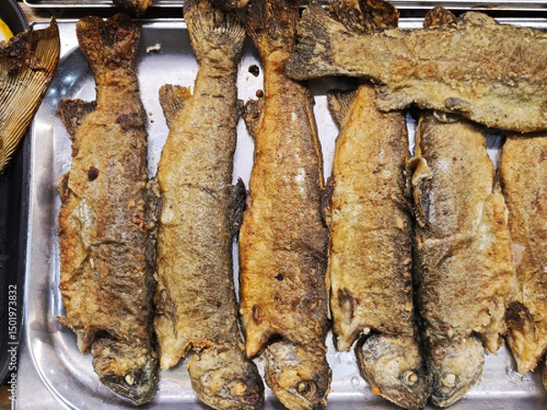 Fototapeta Overhead view of several fried trout, neatly arranged on a metal tray, showcasing a simple yet appetizing culinary presentation