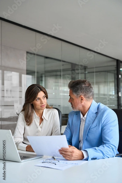 Obraz Finance manager and investor discussing corporate project at meeting. Two busy mature professionals man and woman business leaders checking document talking working on laptop in office. Vertical.