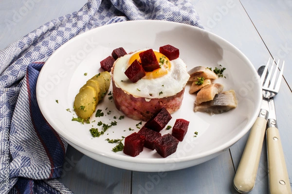 Fototapeta labskaus, north german specialty made with potatoes, beetroot, sour herring, gherkin slices, fried egg and parsley on a plate