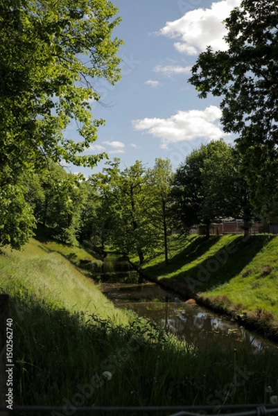 Fototapeta Canal river in summer landscape view. Fresh grass stadswallen with trees horizontal photo.