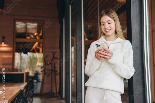 Obraz Young woman using mobile phone while leaning on a door frame
