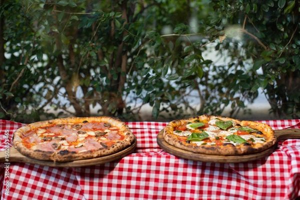 Fototapeta Two freshly baked pizzas on wooden trays with checkered tablecloth.
