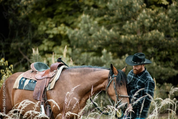 Fototapeta cowboy man with red beard in hat with horse close-up, friendship with animal