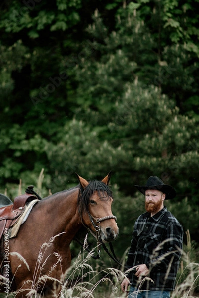 Fototapeta cowboy man with red beard in hat with horse close-up, friendship with animal