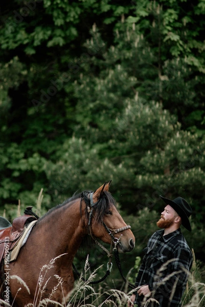 Fototapeta cowboy man with red beard in hat with horse close-up, friendship with animal