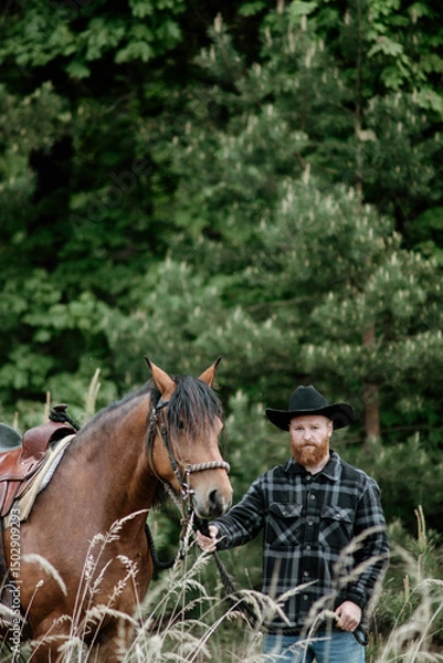 Fototapeta cowboy man with red beard in hat with horse close-up, friendship with animal