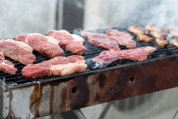 Obraz A barbecue grill filled with different cuts of meat, sizzling and smoking under the sun. Friends gather around, enjoying a summer cookout filled with delicious aromas.