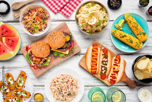 Obraz Summer food table scene with hot dogs, hamburger and sides. Top down view over a white wood background.