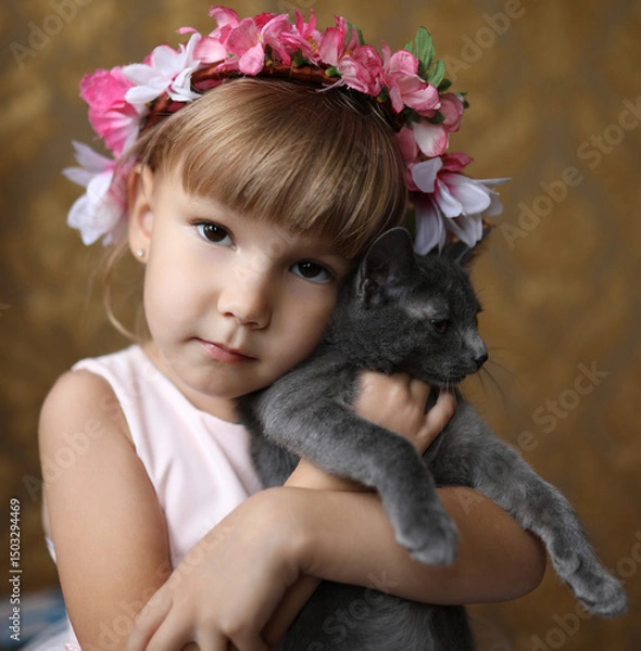 Fototapeta Adorable little girl with a floral crown lovingly hugging a gray kitten. Close-up indoor portrait with warm tones, childhood innocence and pet friendship theme