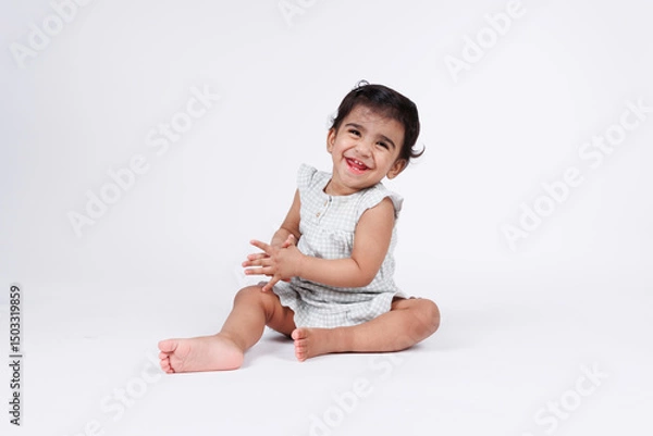 Fototapeta Cute happy little baby girl looking at camera with expression of joy and happiness wearing white dress isolated on white background