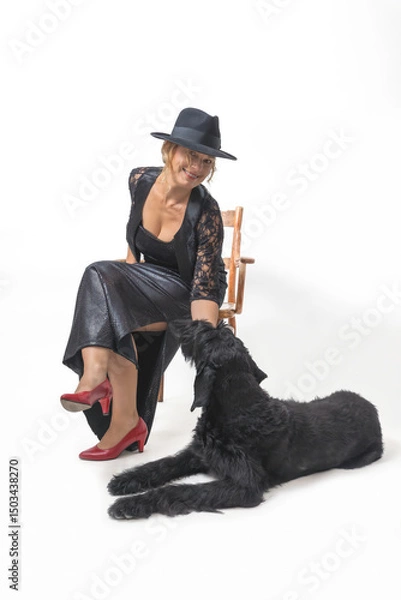 Obraz Middle aged woman is sitting on a chair in a studio. A Big Black Schnauzer dog is lying at her feet.