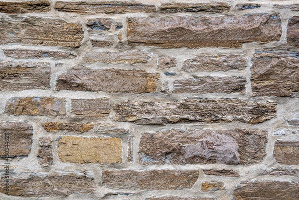 Fototapeta Close-up of a rustic stone wall with rough brown blocks and light mortar. Ideal background texture for architectural, construction, or design-related projects.
