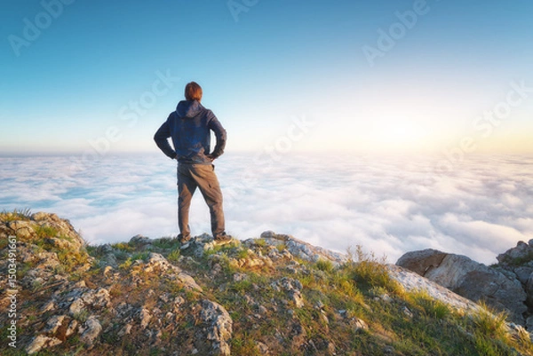 Obraz Man stands over the cover clouds on the edge of the abyss and looks on sun.