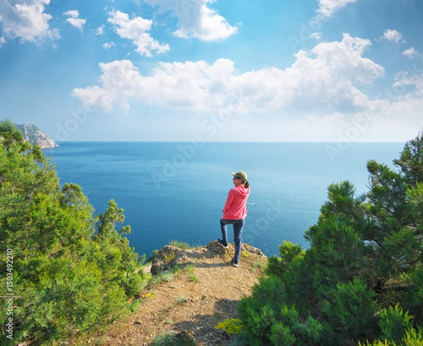 Obraz A girl with a standing on the cliff on the hill and watching the calm sea in the bay.
