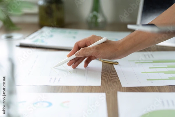 Fototapeta Sustainability and Data Analysis. A close-up of a hand sketching sustainable growth metrics on paper.