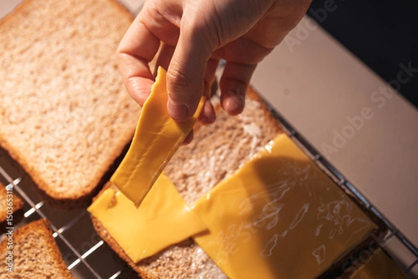 Fototapeta Hand placing a slice of cheese on bread