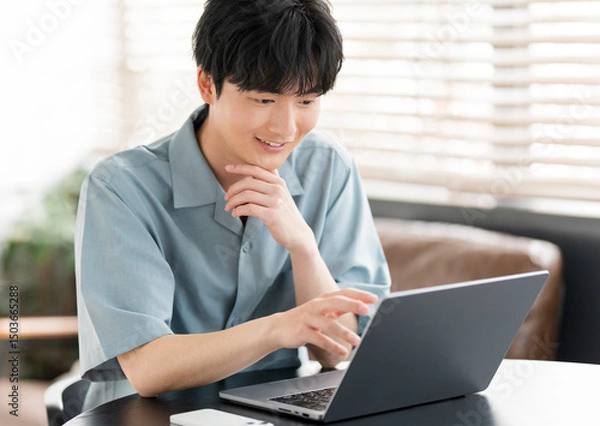 Obraz 若い日本人男性がノートパソコンを開き作業をしている。