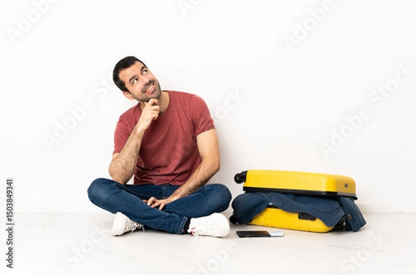 Fototapeta Caucasian handsome man with a suitcase full of clothes sitting on the floor at indoors and looking up