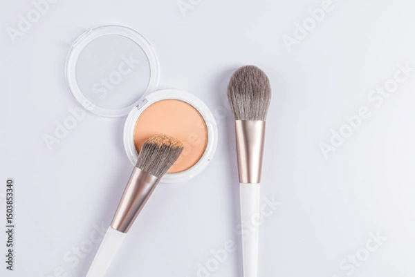 Fototapeta A chic compact powder in a white round package, two white professional makeup brushes on a white background. top view. cosmetic background for design.