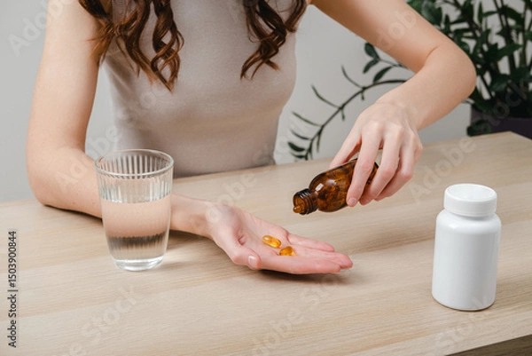 Fototapeta A woman holds omega-3 fish oil capsules. Healthy lifestyle, prevention and treatment of diseases. The woman takes and drinks dietary supplements and vitamins for skin, nails and hair. 
