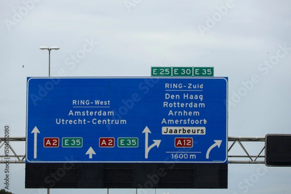 Fototapeta Blue direction sign Amsterdam on the A2 motorway and junction to A12 Rotterdam and Den Haag