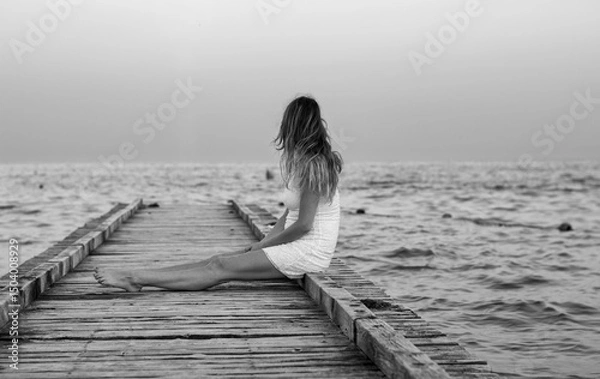 Obraz the woman in meditation sitting on the pier in front of the sea at sunset