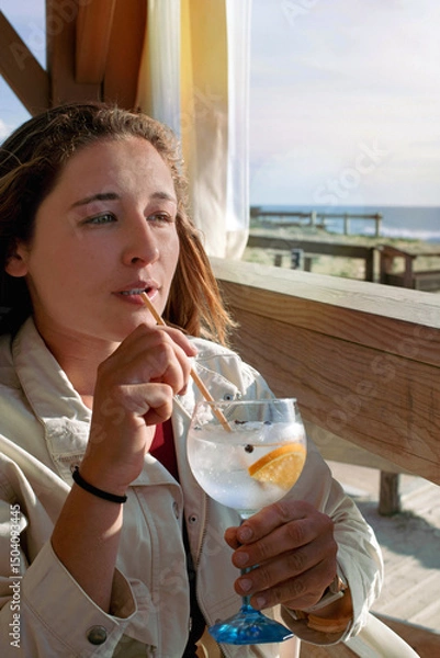 Obraz Beautiful young woman drinking a gin and tonic on a terrace.