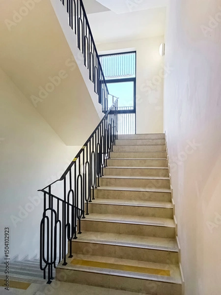 Fototapeta Detail of a flight of stairs with concrete steps and iron railings inside a building. Close-up, vertical photograph.