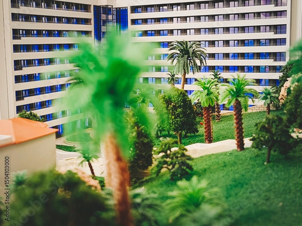 Fototapeta A model of a multi-story modern house surrounded by artificial trees and a lawn. Close-up, selective focus.