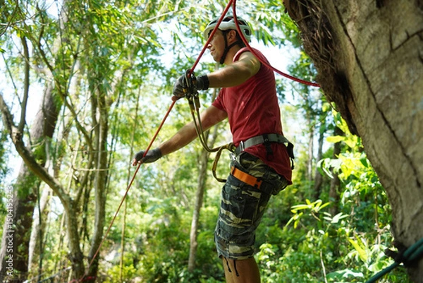 Fototapeta A man is walking across a challenging ropes course in the extreme park