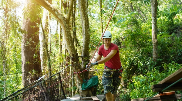 Fototapeta A man is walking across a challenging ropes course in the extreme park