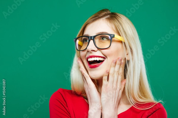 Obraz Laughing Girl in Eyeglasses and Red Top on Green Background. Closeup Portrait of Young Blonde with Long Hair and Charming Smile in Studio.