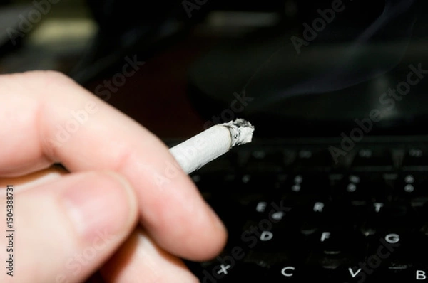 Fototapeta Close-up of hand holding cigarette over a computer keyboard