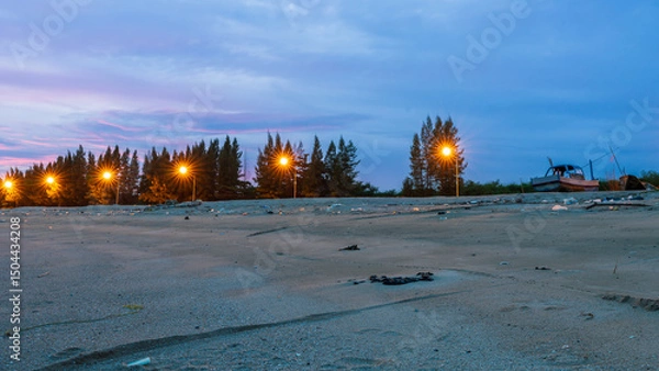 Fototapeta Photo of a beach full of trash in the evening with a beautiful red sky and clouds and sparkling lights illuminating the night street.