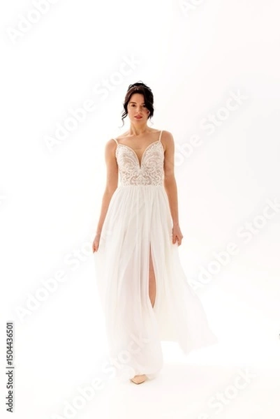 Fototapeta Model walks gracefully in a flowing white dress showcasing elegance and beauty in a softly lit studio setting